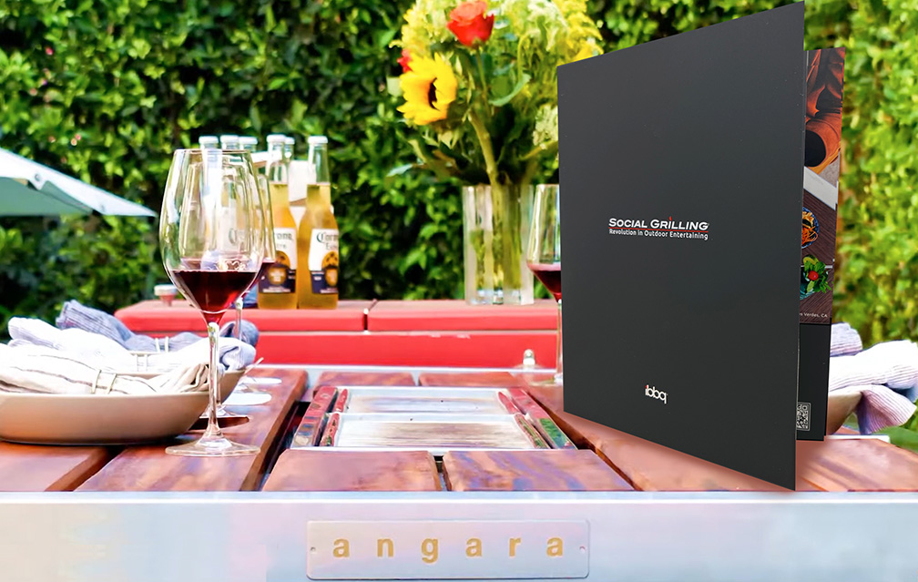 Composite image of iBBQ's presentation folder superimposed on an image of their Angara BBQ table