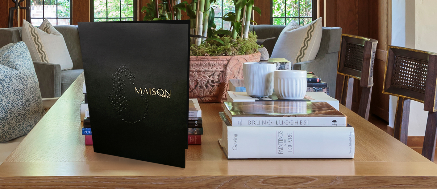 Composite image of presentation folder superimposed on tabletop in dining room designed by Maison, Inc.